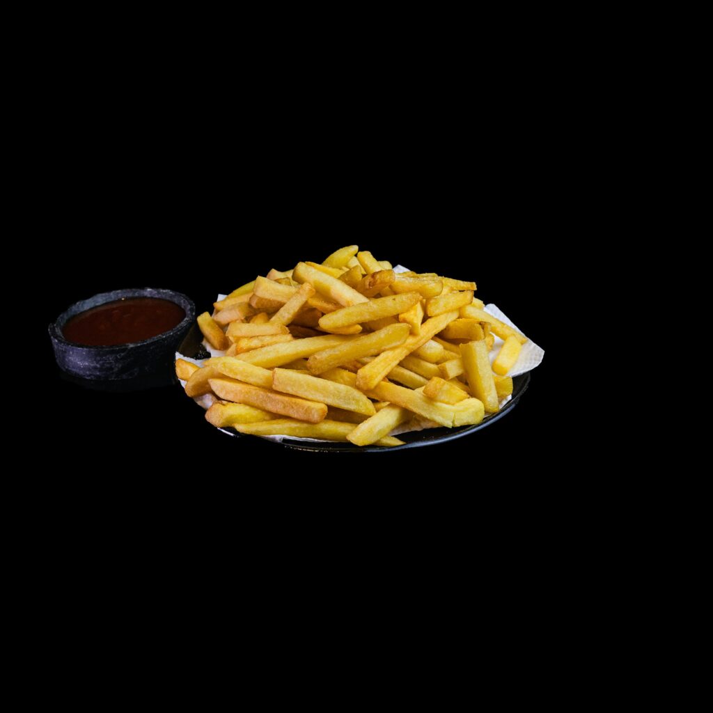 Crispy golden French fries served with tangy ketchup, isolated on black background.